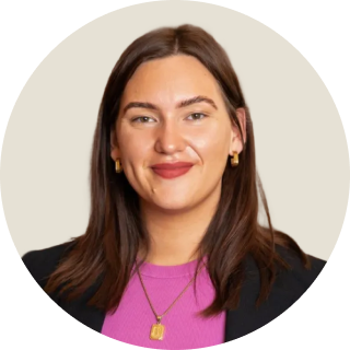 Smiling woman with straight brown hair wearing a blazer, pink top and gold jewellery.